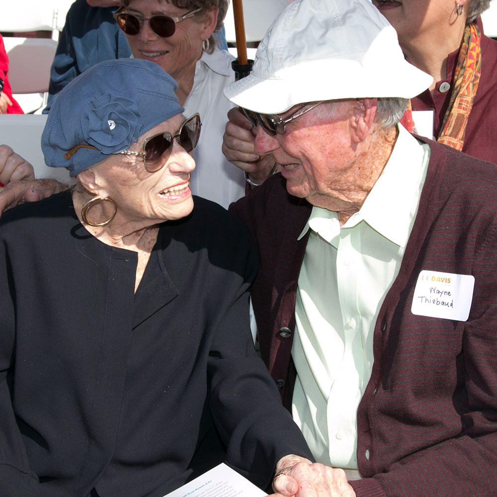 Photo of older woman and man seated and holding hands.