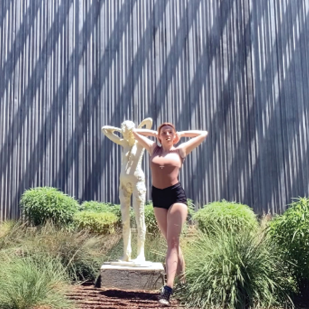 Woman dancing in front of statue of a woman by the museum.