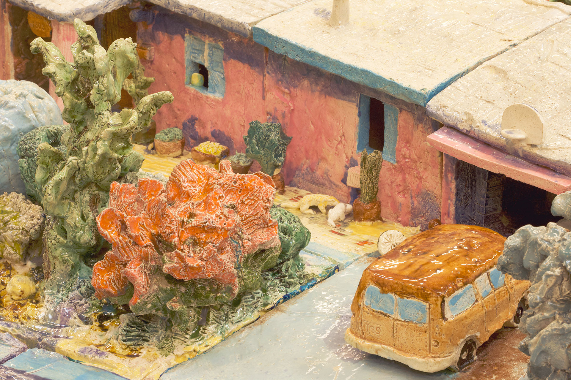 Close up of ceramic house showing a tan van in the driveway and various colored plants.